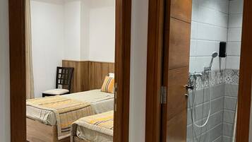 A hotel room with a bed, a wooden headboard, a shower area with a tiled wall, and a wooden door.