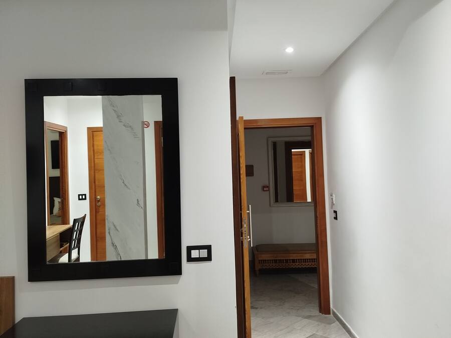A hallway with a black-framed mirror, a wooden bench, and a trash bin.