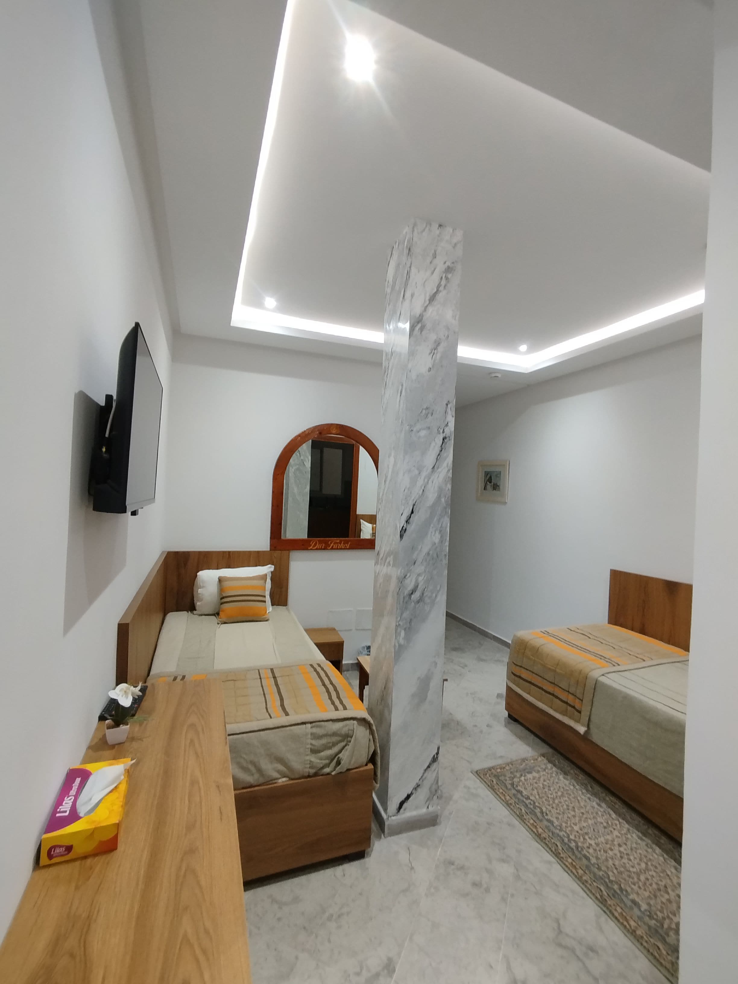 Une chambre moderne avec un lit en bois, un pilier en marbre et un téléviseur à écran plat fixé au mur.