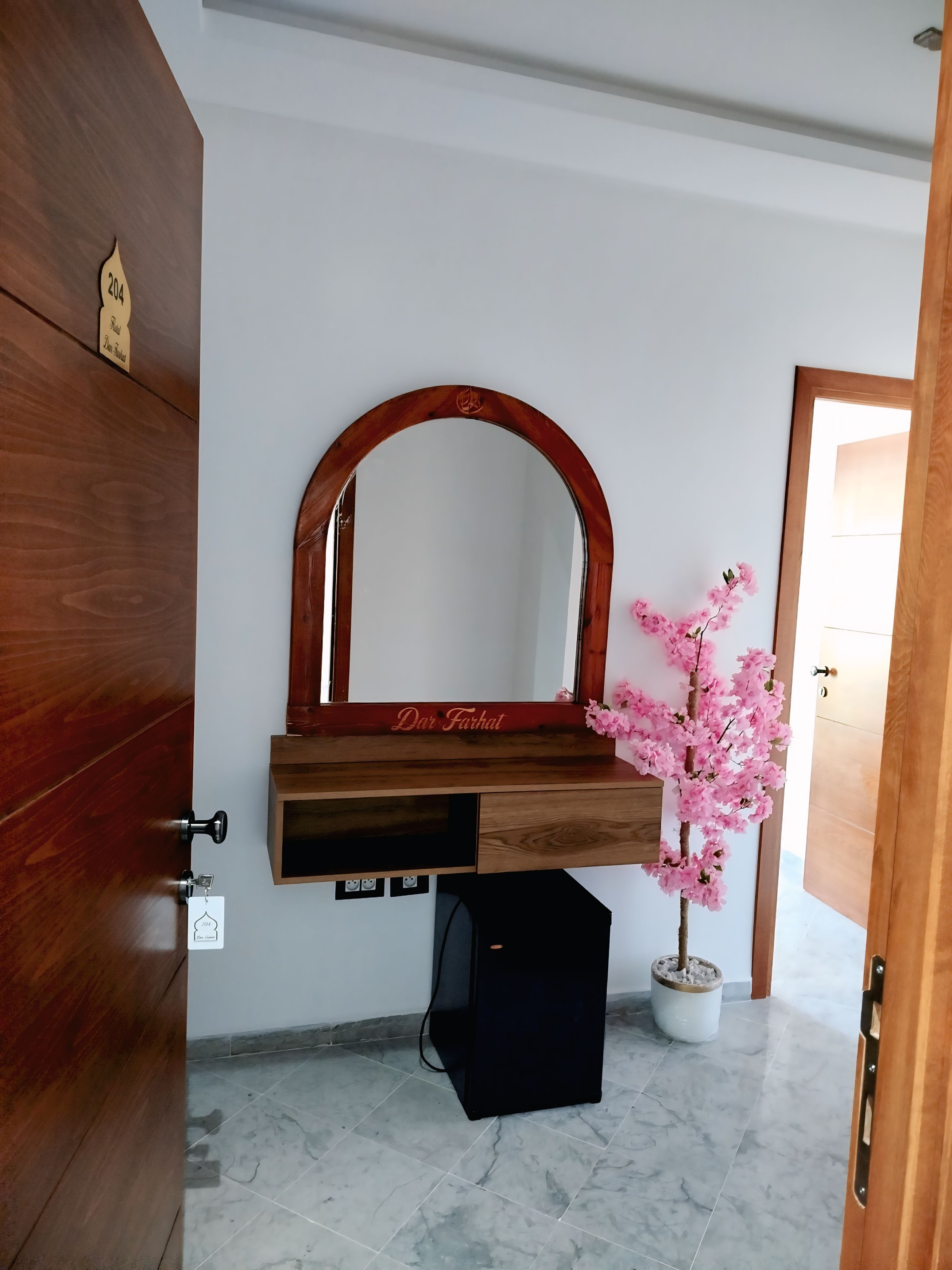 A room with a wooden wardrobe, a mirror with a wooden frame, a small potted plant, and a door.