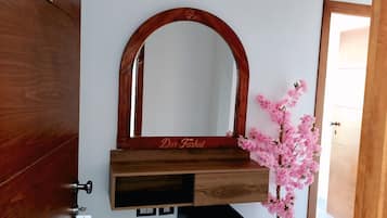 A room with a wooden wardrobe, a mirror with a wooden frame, a small potted plant, and a door.