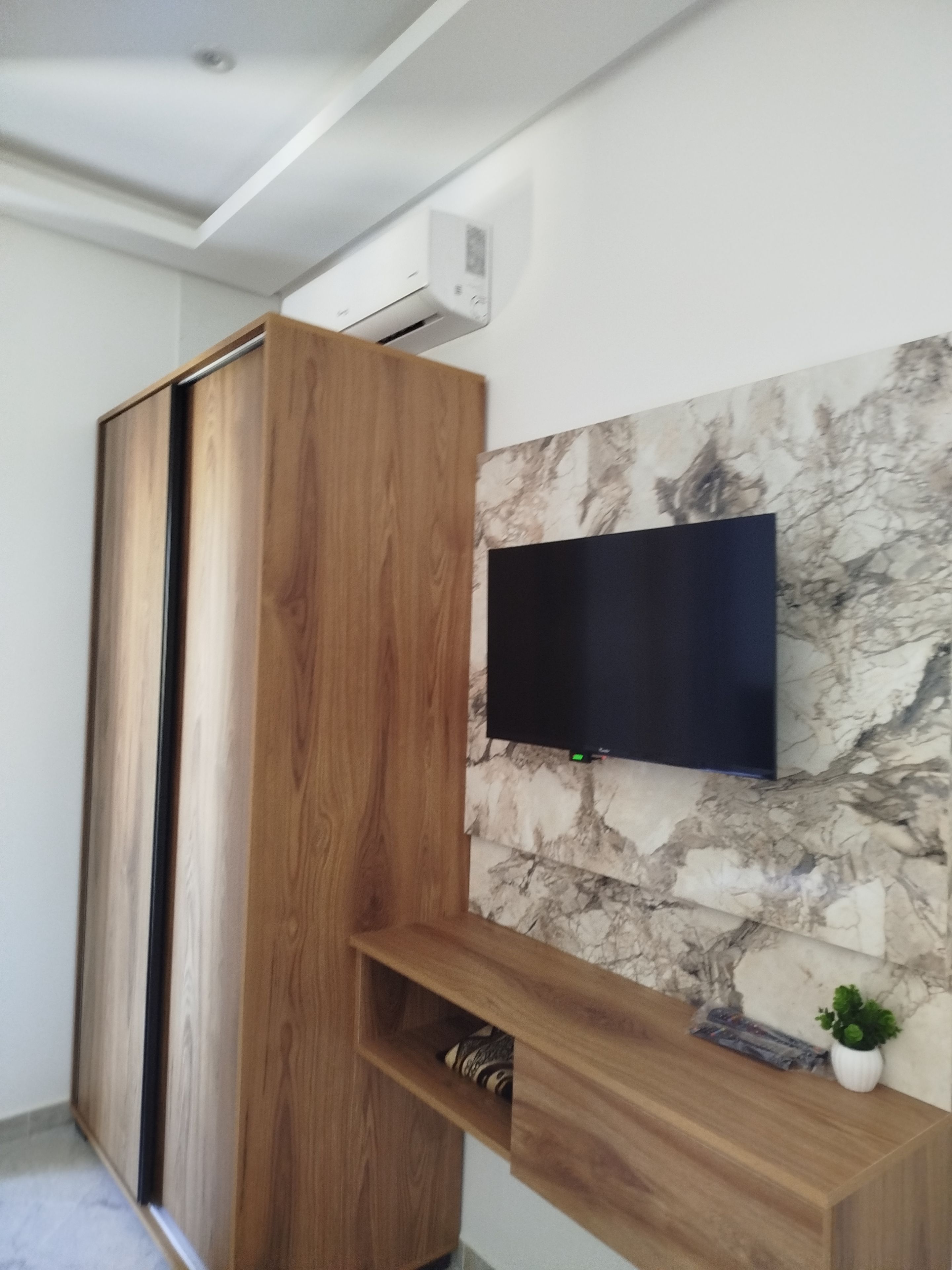 Una habitación moderna con un armario de madera, un televisor de pantalla plana montado en la pared y un revestimiento mural con diseño de mármol.