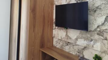 Una habitación moderna con un armario de madera, un televisor de pantalla plana montado en la pared y un revestimiento mural con diseño de mármol.