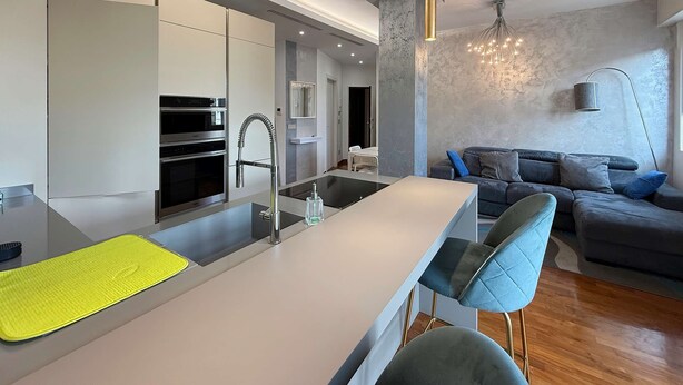 Una cucina moderna con isola centrale, elettrodomestici integrati e zona pranzo con divano grigio e sedie blu.