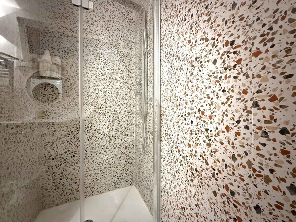 A modern bathroom with a terrazzo floor, a glass shower enclosure, and a visible hand dryer.