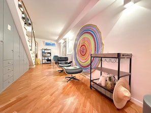 A modern interior with a wooden floor, a large abstract painting, a bookshelf, and a staircase.