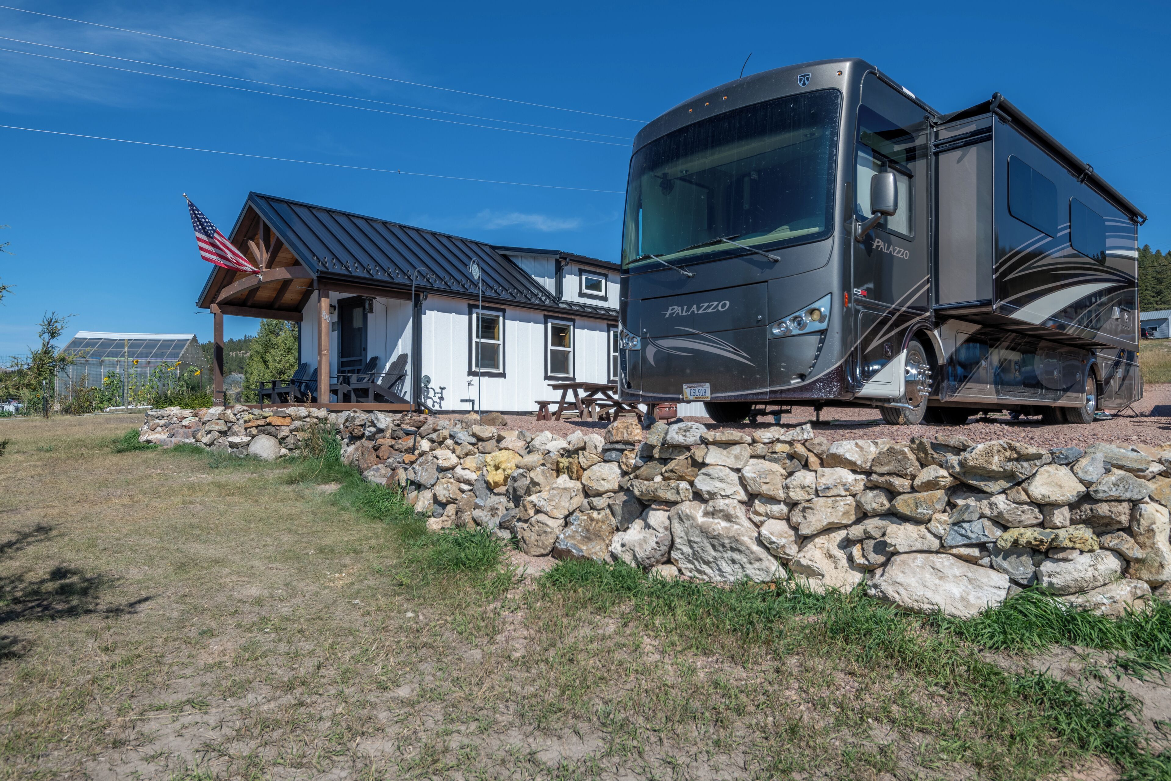 Un camping-car moderne est garé à côté d’une maison dont les fondations sont en pierre et le toit en métal.