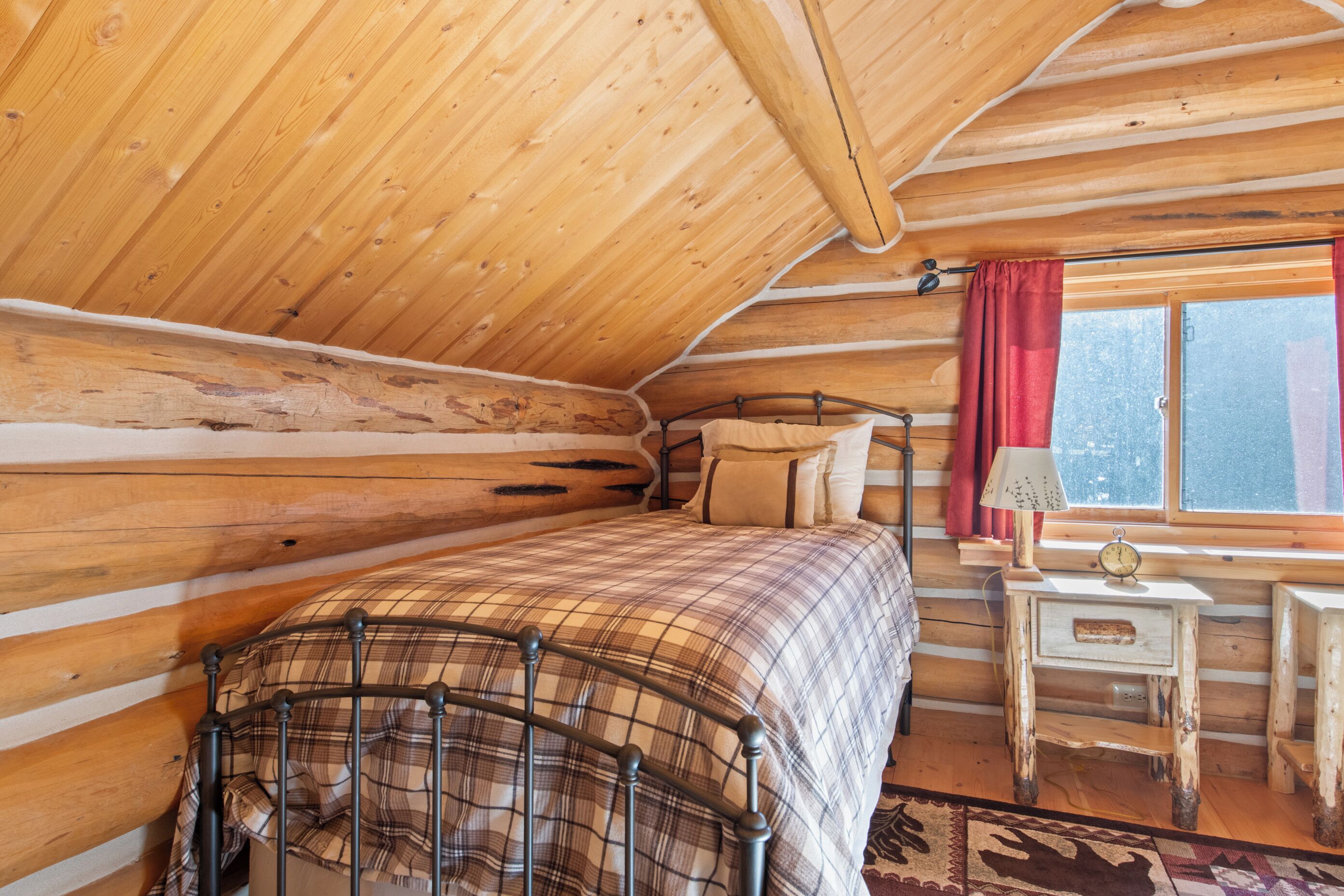 A cozy log cabin bedroom with a bed, a nightstand, and a window with curtains.