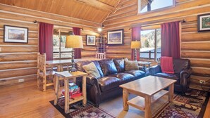 A log cabin interior with a wooden floor, leather sofa, wooden coffee table, and a dining table with chairs. - Stony Creek Lodge-Famous Rock Creek MT! 4 seasons! (Philipsburg)