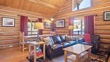 L’intérieur d’une cabane en rondins, avec un plancher en bois, un canapé en cuir, une table basse en bois et une table à manger avec des chaises.