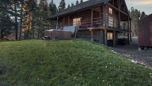 A log cabin with a hot tub and outdoor seating area, surrounded by a grassy yard and trees. - Stony Creek Lodge-Famous Rock Creek MT! 4 seasons! (Philipsburg)