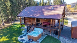 A wooden cabin with a hot tub and deck, surrounded by a forest. - Stony Creek Lodge-Famous Rock Creek MT! 4 seasons! (Philipsburg)
