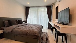 Ein modernes Hotelzimmer mit einem großen Bett, einem Schreibtisch mit Flachbildfernseher und einem großen Fenster mit Vorhängen.