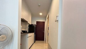 Ein enger Flur mit einer Küchenzeile links, ausgestattet mit weißen Schränken, einer schwarzen Arbeitsplatte und einem Kühlschrank.