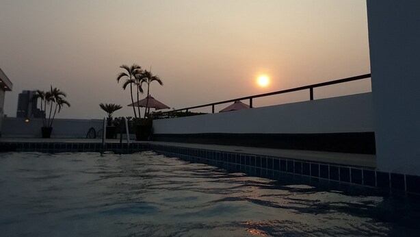 Ein Poolbereich mit Sonnenuntergang im Hintergrund, Palmen und einem Gebäude mit Balkon.
