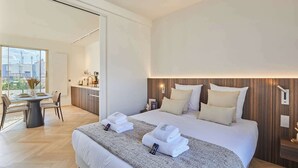 A modern hotel room with a large bed, bedside tables, a small desk, and a view of the city through large windows.