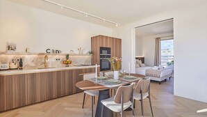 A modern kitchen with a wooden island, a dining area with a table and chairs, and a living room with a sofa and a view of the city.