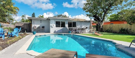 A backyard with a swimming pool, patio furniture, and a small house.