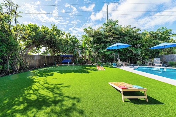 A backyard with a swimming pool, artificial grass, a wooden deck, and a wooden fence.