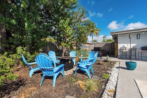 An outdoor seating area with blue chairs and a table, surrounded by a garden and a wooden fence.