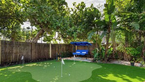 Un jardin avec une pelouse artificielle, une clôture en bois et un parasol bleu.