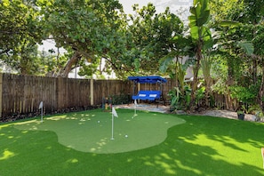 Un jardin avec une pelouse artificielle, une clôture en bois et un parasol bleu.