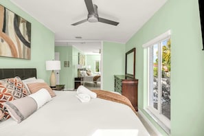 A bedroom with a bed, a ceiling fan, a window, and a nightstand with a lamp.