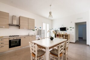 Una cucina moderna con elettrodomestici integrati, un'area pranzo con tavolo e sedie bianche e un televisore montato a parete.