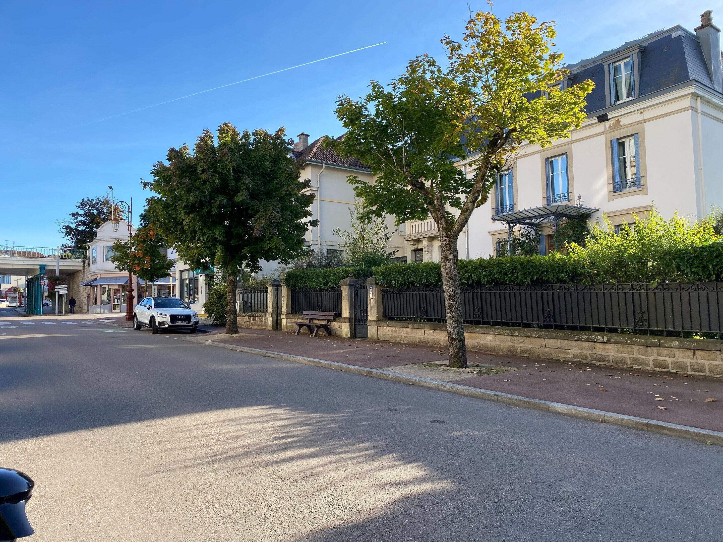 A residential street with houses, a white car parked on the side, and a bench along the sidewalk.