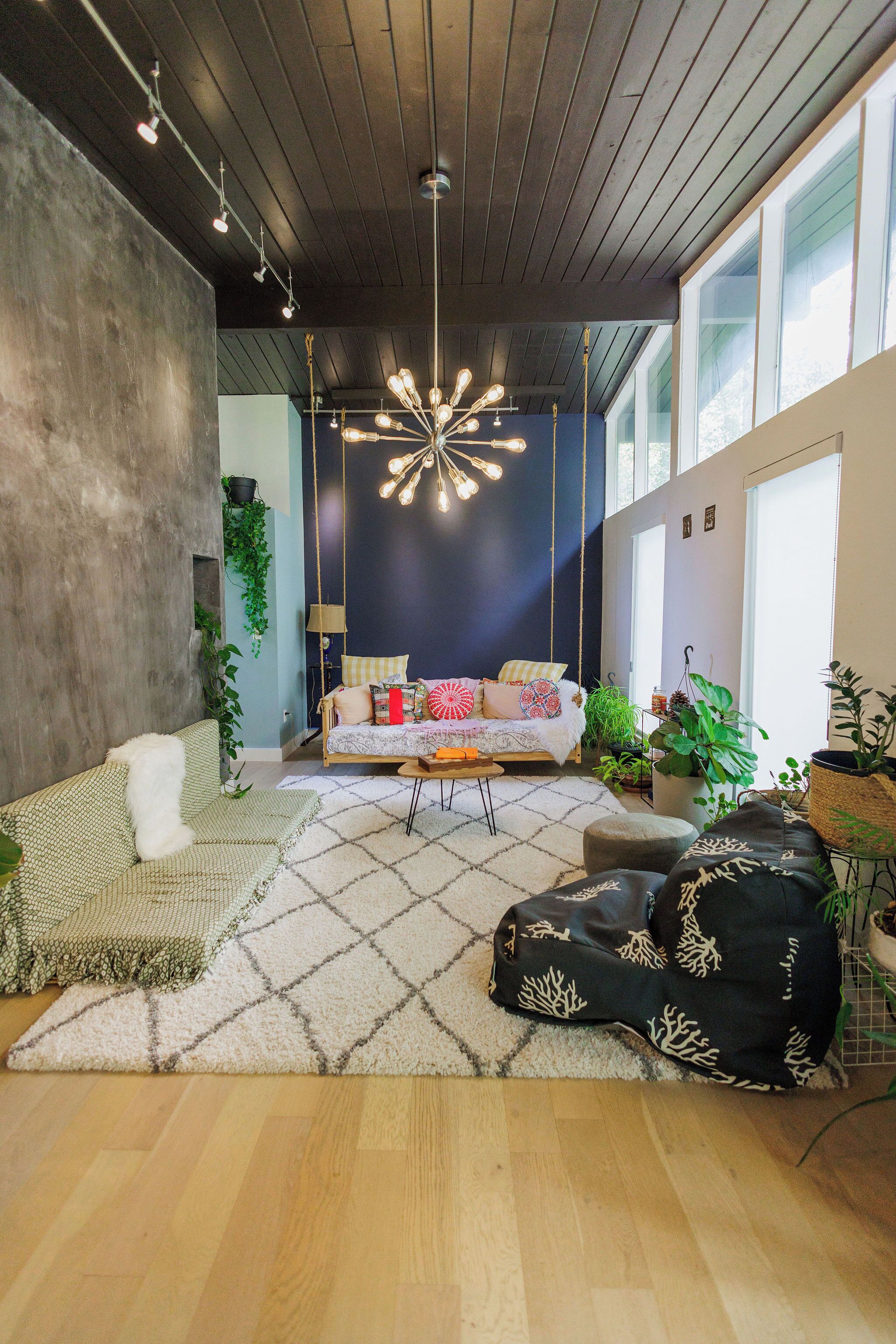 Una sala de estar moderna con un sillón colgante, un sofá y una mesa de centro. Hay plantas y una lámpara colgante.