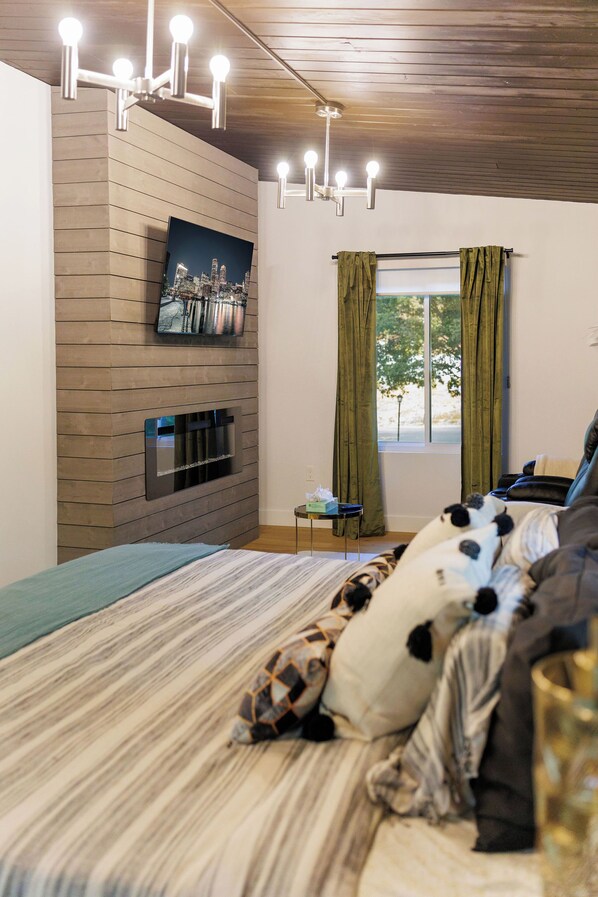 A bedroom with a bed, a TV mounted on the wall, a window with curtains, and a ceiling light fixture. - Mid-Century Modern x Bohemian Home (Natick)