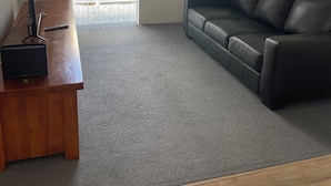 A room with a wooden desk, a black leather sofa, and a large window with blinds. - Comfortable Getaway for Families & Groups (Byford)