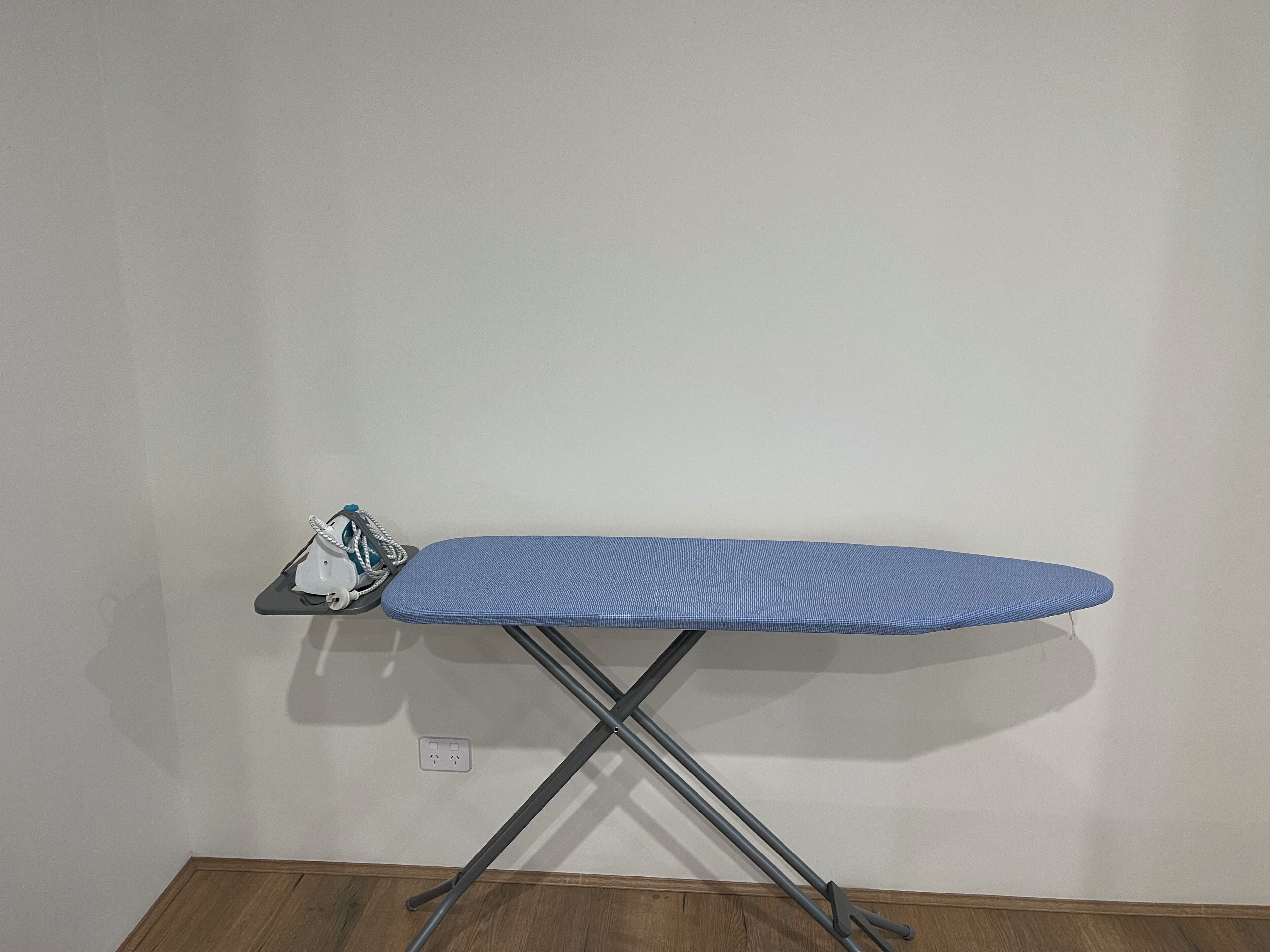 Une planche à repasser bleue, dotée d’une structure en métal et d’un porte-pinces à linge blanc.