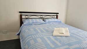 A neatly made bed with a blue and white patterned bedspread and pillows, a folded white towel on the bed, and a black metal headboard. - Comfortable Getaway for Families & Groups (Byford)