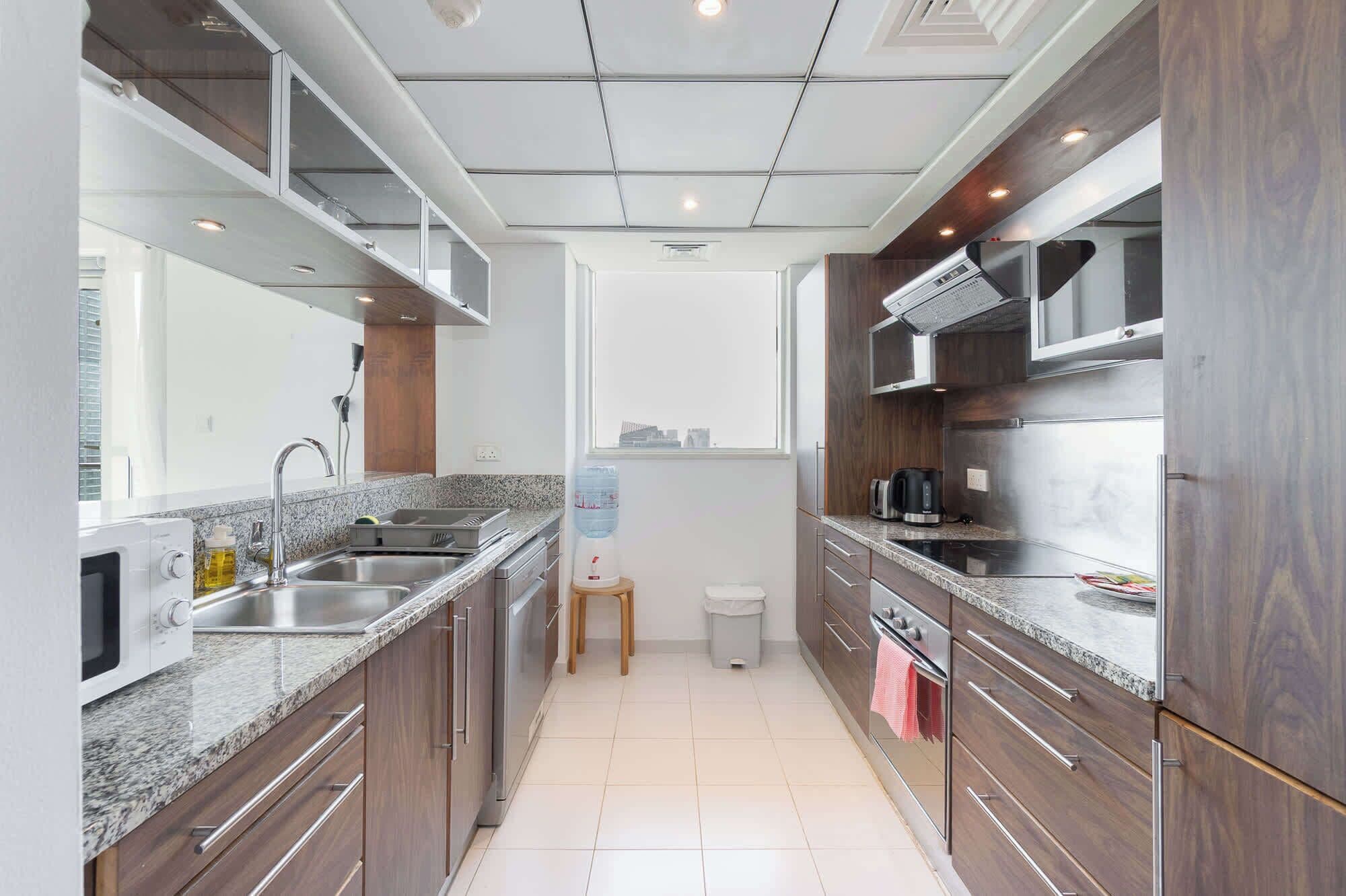 Een moderne keuken met granieten aanrechtbladen, roestvrijstalen apparatuur en houten kastjes.