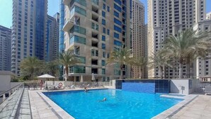 A swimming pool surrounded by high-rise buildings, with palm trees and lounge chairs. - StayShort - Dubai Marina sleeps 4 with Marina Views! (Dubai Marina)