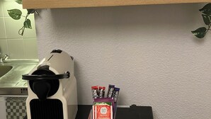 Een keuken met een koffiezetapparaat, een klok en een plank met potten en een plant.