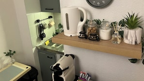 Een keuken met een klok, een waterkoker, potten en een plank met planten.