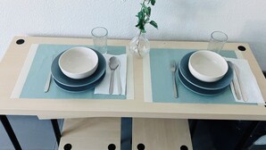 Een eettafel gedekt met borden, kommen, bestek en glazen, met een plant in het midden.