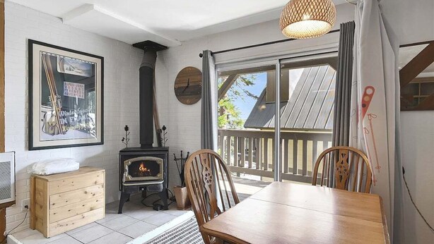 Quarto acolhedor com uma mesa de madeira, cadeiras, lareira e uma grande janela com vista para o exterior.