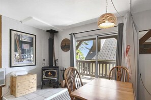 Een gezellige kamer met een houten tafel, stoelen, een open haard en een groot raam met uitzicht.