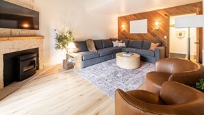 Un salon moderne avec une cheminée, un canapé d’angle, une table basse ronde et des fauteuils en cuir.