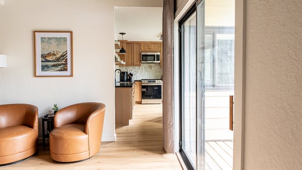 Un salon moderne avec des fauteuils en cuir, un tableau encadré et une vue sur la cuisine.