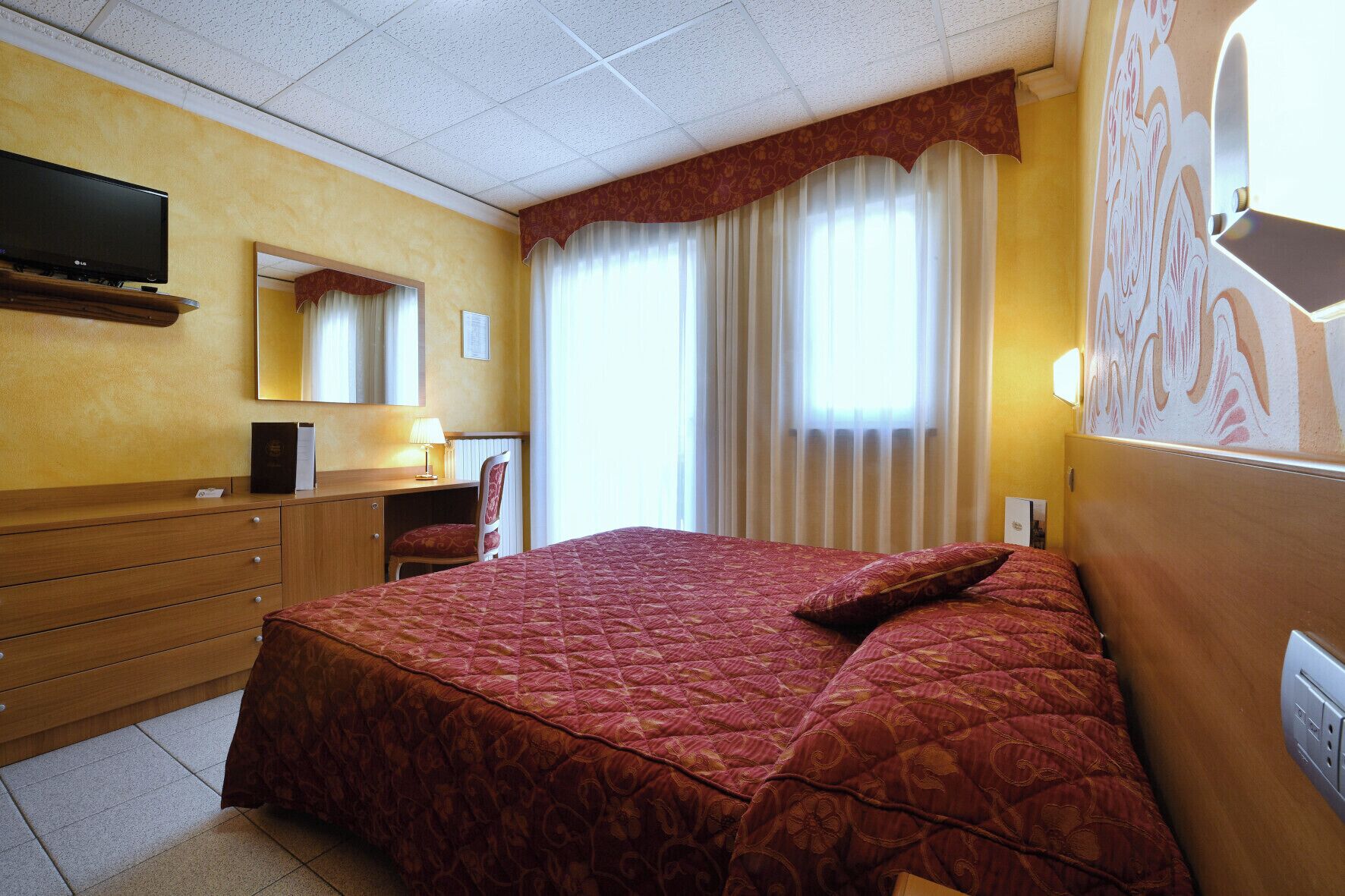 A hotel room with a large bed, a desk with a chair, a television, and a window with curtains.