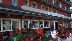 A hotel with a red facade, multiple windows, and outdoor seating with white tables and chairs. - Stella Alpina Hotel e Ristorante (Druogno)