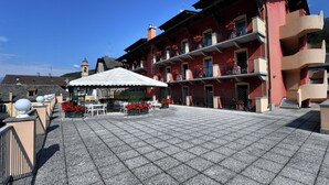 A courtyard with a covered seating area, a building with balconies, and a clock tower in the background. - Stella Alpina Hotel e Ristorante (Druogno)