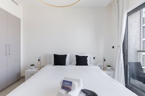 A modern hotel room with a large bed, white bedding, two bedside tables with lamps, a small plant, and a view of the city through a large window. - Meydan One Sleeps 5 With Great Amenities (Dubai)