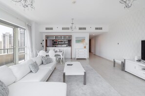 A modern living room with a white sofa, a coffee table, and a TV stand. - Dubai Marina Sleeps 4 With Marina Views (Dubai)