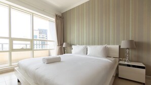 Habitación de hotel con una cama grande, dos mesitas de noche, un ventanal con cortinas y una pared a rayas.