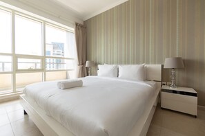 A hotel room with a large bed, two bedside tables, a window with curtains, and a striped wall. - Dubai Marina Sleeps 4 With Marina Views (Dubai)